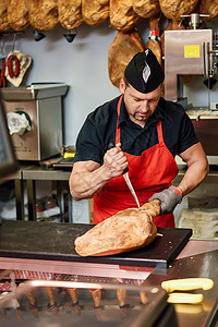 男屠夫用金属安全网手套家现代肉店里烤火腿屠夫家现代化的肉店里烤火腿背景图片