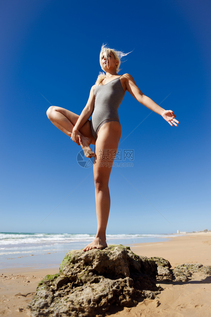 高加索女人海滨练瑜伽年轻的女站条腿上,边练树的姿势,西牙的卡迪兹安达卢西亚的个宁静的海滩上高加索金发图片