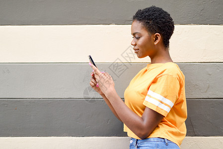 年轻的黑人妇女户外用她的智能手机生活方式的头发很短的女孩穿着休闲服年轻的黑人妇女户外用她的智能手机背景图片