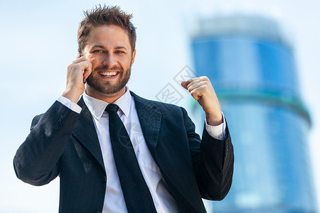 成功的商人,男执行商人他的手机上交谈,个现代城市的个高层办公大楼前庆祝图片