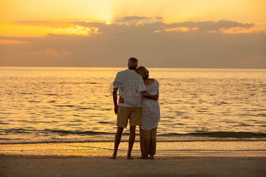 老年男女夫妇日落或日出时拥抱荒芜的热带海滩上图片