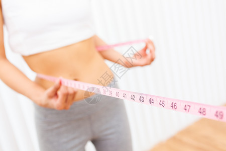 年轻女孩用粉红色的卷尺测量她的腰部或腰围背景图片