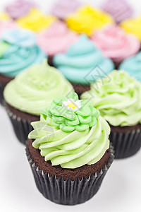 巧克力杯蛋糕与糖霜,粉红色,紫色,蓝色,黄色绿色白色背景上拍摄图片