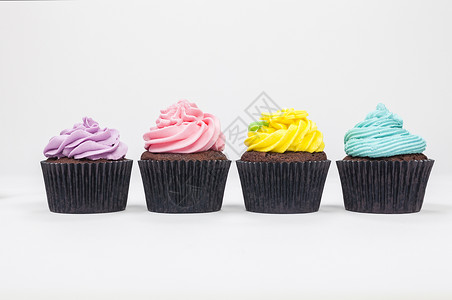 四个巧克力杯蛋糕与糖霜或霜,粉红色,紫色,蓝色黄色与绿叶,拍摄白色背景图片