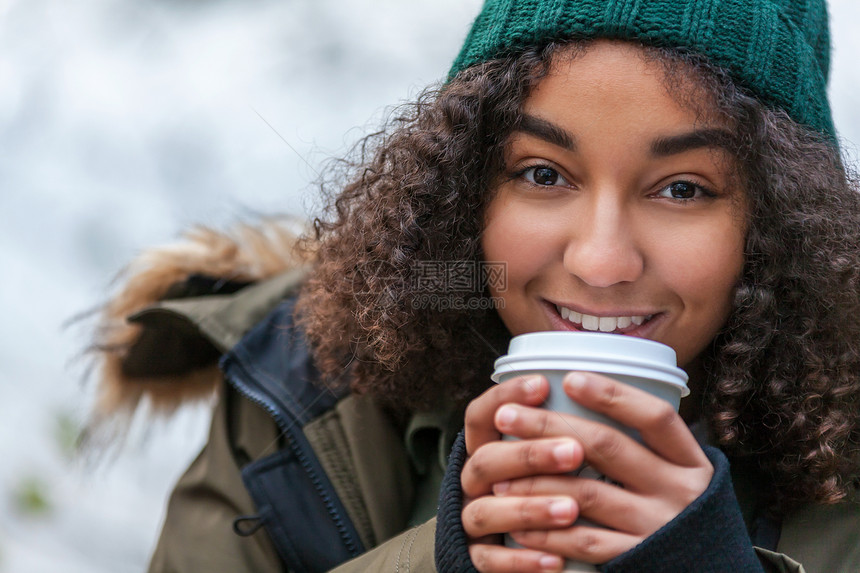 美丽快乐的混合种族非裔美国女孩十几岁的女青年,微笑着喝着外卖咖啡,外面戴着绿色的帽子外套图片