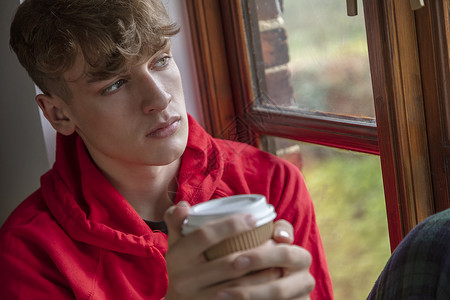 悲伤沮丧体贴的青少年男孩男青少年年轻人看着窗外喝咖啡或茶图片