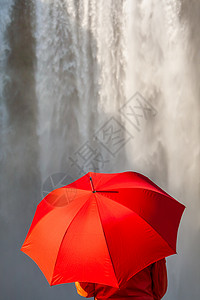 穿着红色外套夹克的轻女子,瀑布前着把红色的伞图片