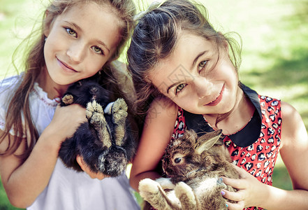 两个快乐的女孩拥抱毛茸茸的兔子图片