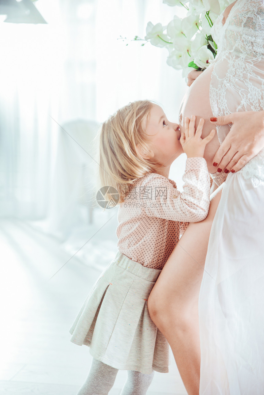 小女儿亲吻她怀孕的母亲的肚子图片