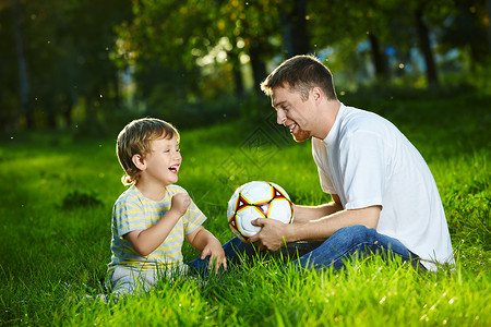 父子俩说话,坐公园里踢足球背景图片
