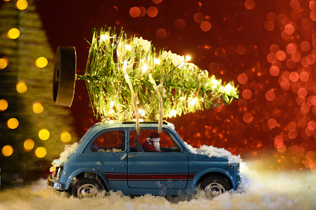 圣诞老人穿着蓝色复古玩具车,节日背景上送圣诞或新年照明树圣诞老人送圣诞或新年树背景图片