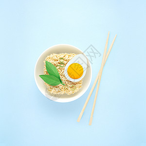 创意食物饮食健康饮食照片,美味拉面面条意大利面与鸡蛋,绿色筷子碗蓝色背景图片