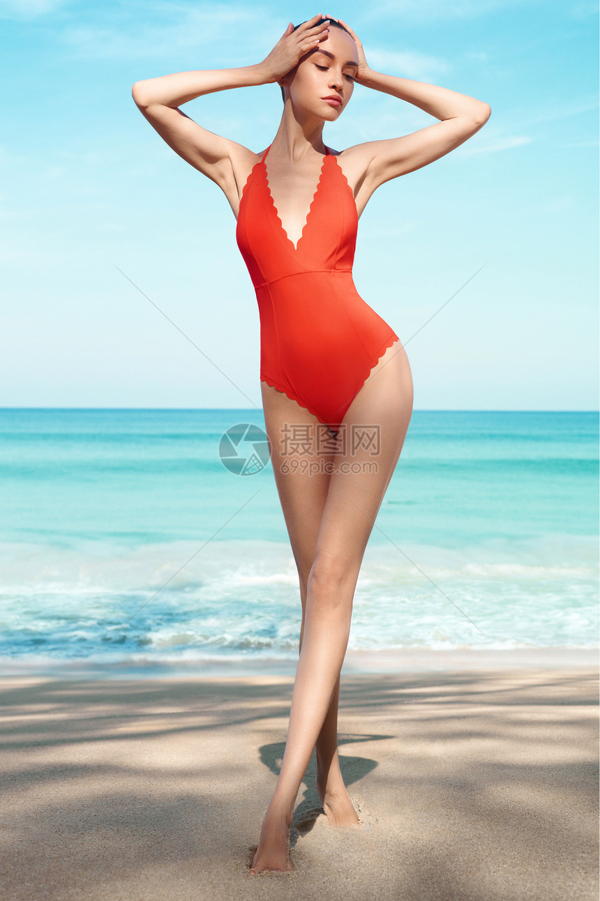 热带海滩上美丽感的女士时尚的女人,苗条完美的身材走蓝海前模特穿着红色泳装海洋附近放松年轻日光浴美女的肖像图片