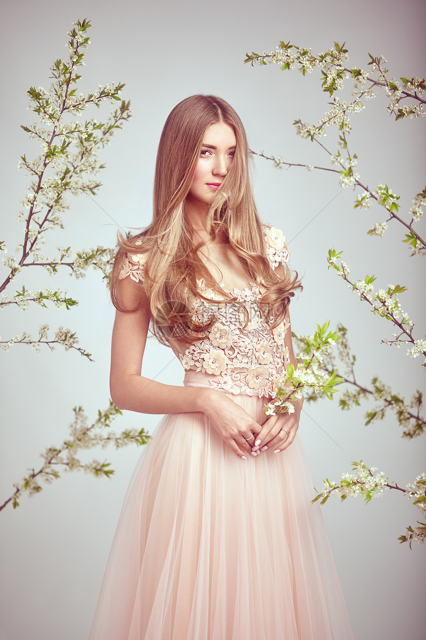 穿着蕾丝婚纱的漂亮女人美丽的女士,健康美丽的头发模型摆棵盛开的苹果树的背景上春天的照片图片