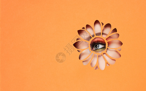 橙色眼睛年轻美丽的女人的眼睛有着明亮的粉红色阴影富有表现力的眉毛,用橙色的纸看着花朵形状的图案非洲菊花夏天的图案广告横幅背景