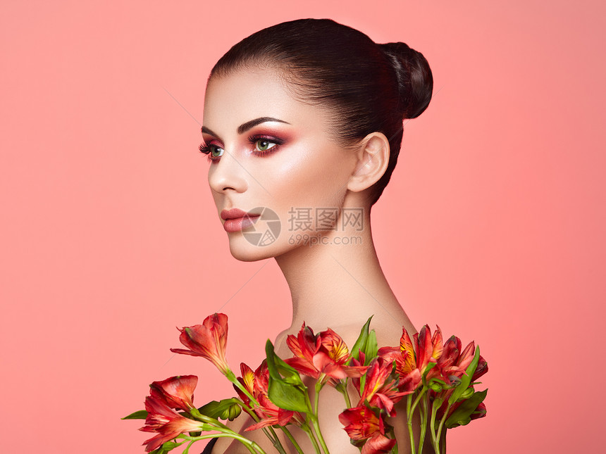 美丽的年轻女人的肖像与阿斯特拉米里亚花黑发女人,化妆豪华完美的皮肤睫毛化妆品眼影红花珊瑚色图片