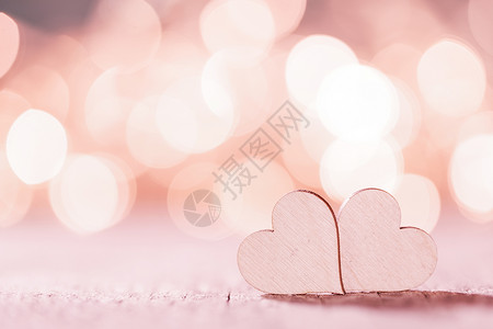 两颗手工制作的粉红色木心明亮的灯光背景下波基背景上的粉红色心脏背景