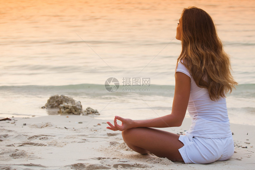 年轻健康的女人日落时海滩上练瑜伽日落时海滩上的瑜伽女人图片