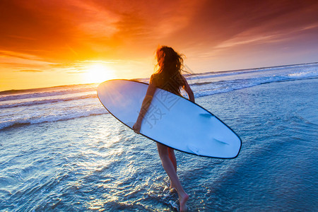 位美丽的年轻苗条的运动女穿着比基尼,穿着冲浪板,日落时站海边有冲浪板的女人背景图片