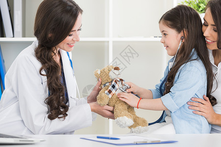 快乐的母亲孩子与泰迪熊听诊器儿科医生办公室儿科医生办公室的母亲孩子图片
