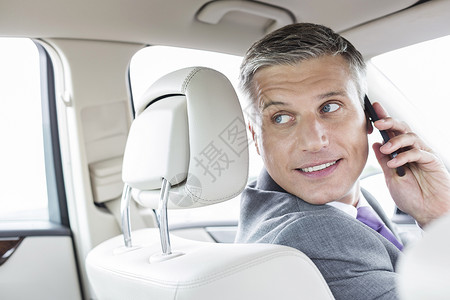微笑的成熟商人坐车里用智能手机说话图片