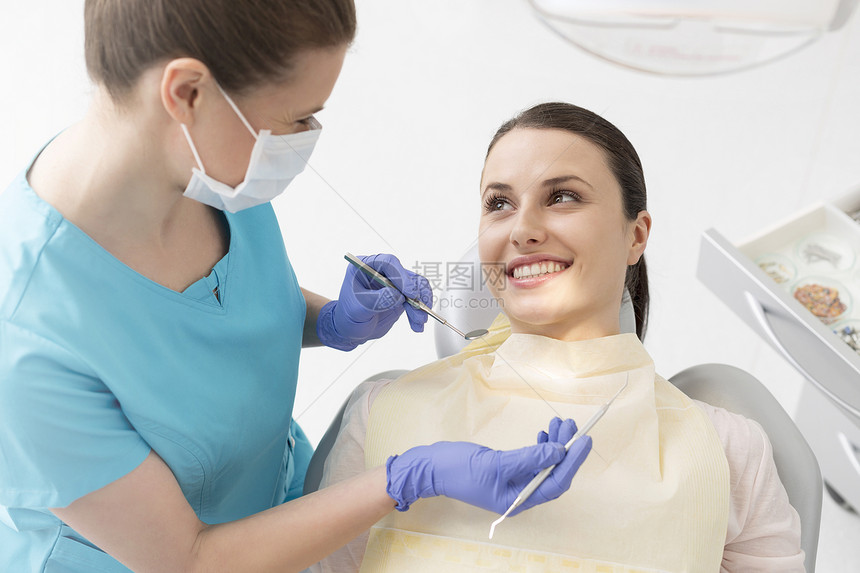 微笑的年轻病人看着临床上有牙科设备的女牙医图片
