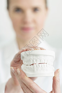 临床上持白色假牙的女牙医的特写图片