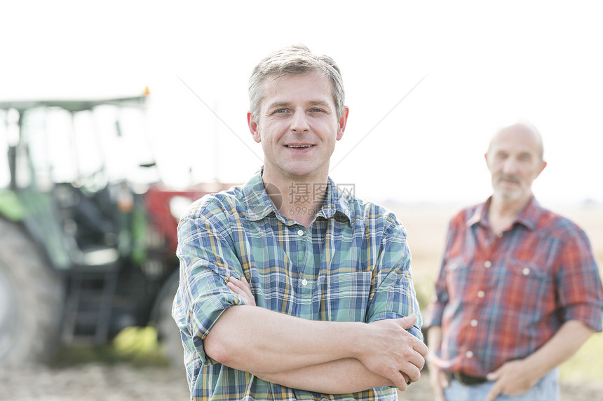 成熟农民的肖像与农场的同事交叉图片