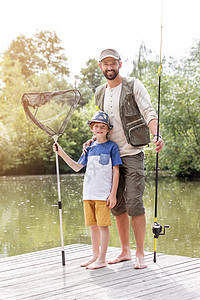 全长的肖像,微笑的父亲儿子站码头上钓鱼,靠湖高清图片