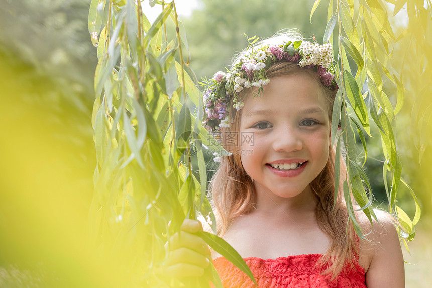 微笑可爱的女孩的肖像,穿着鲜花站公园的树叶中图片