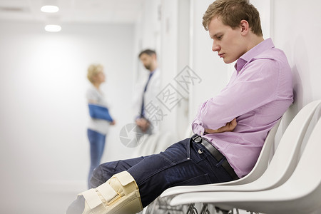 男人坐医院候诊室里看着膝盖上的支撑图片