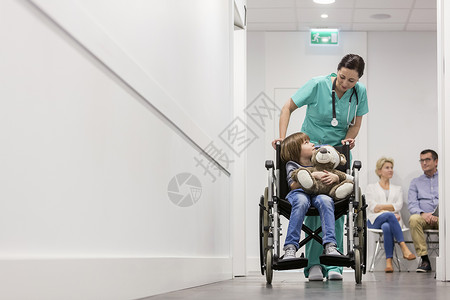 护士推着带泰迪熊的男孩坐轮椅上,病人医院走廊等着图片