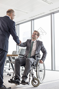 商人与微笑的残疾同事握手,着办公室会议室的窗户图片