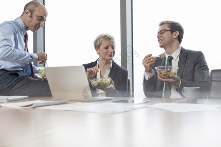 微笑的商业同事办公室开会时坐会议室吃午饭图片