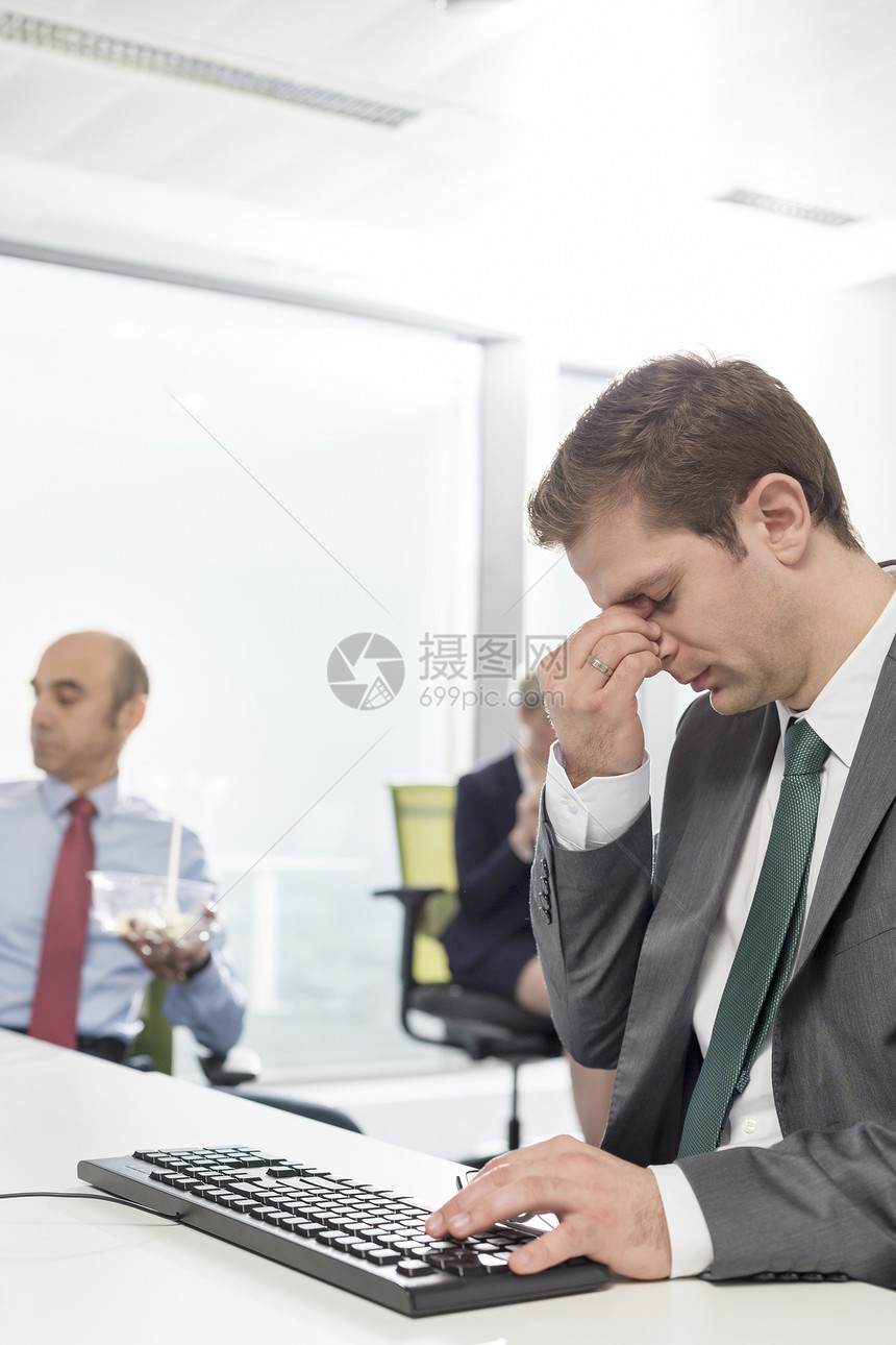 疲惫的商人坐现代办公室的办公桌前图片
