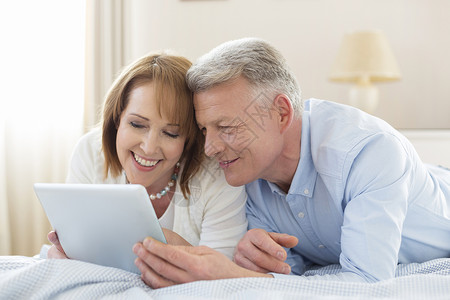微笑的成熟夫妇分享数字平板电脑,而躺床上家图片