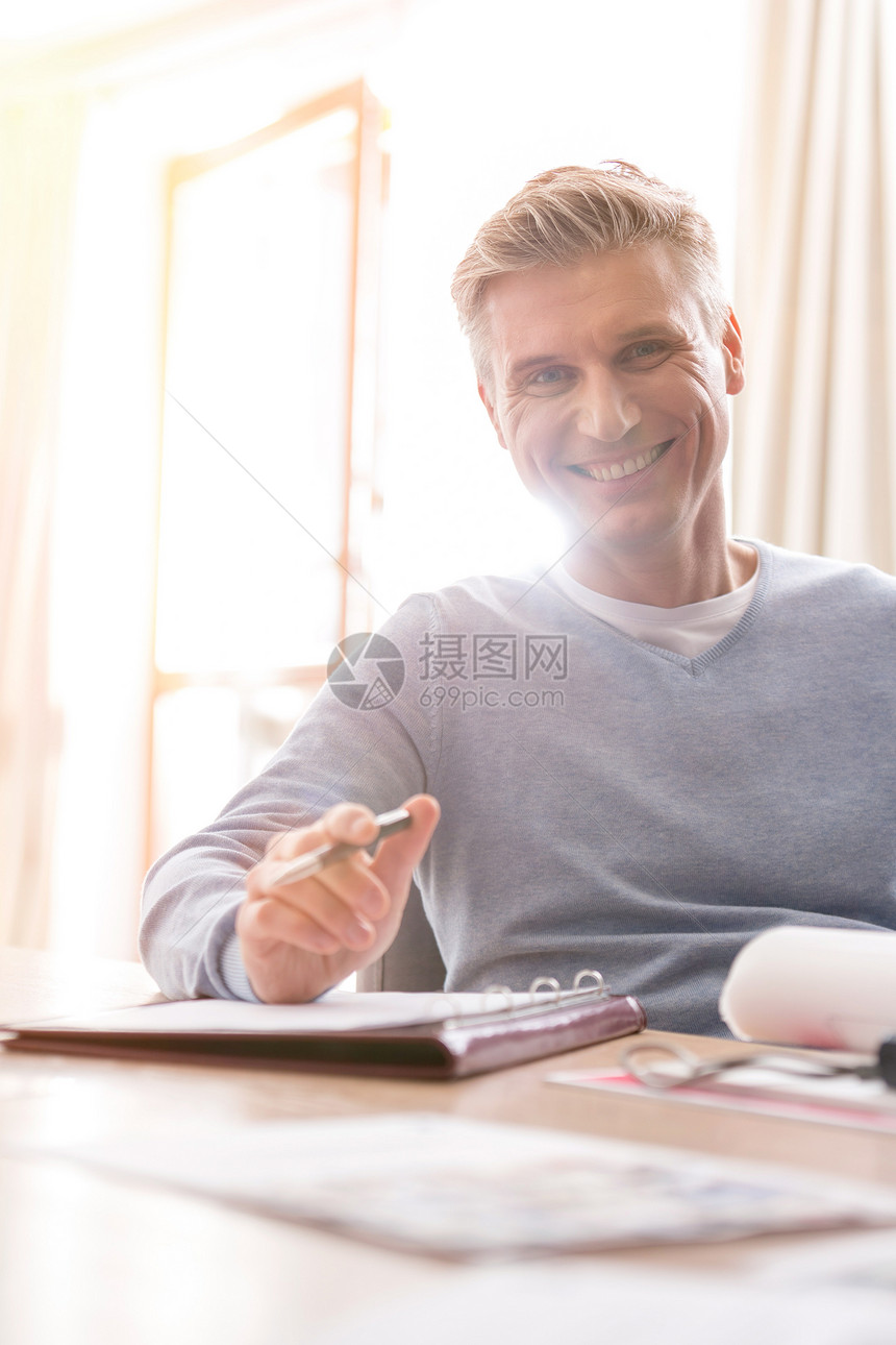微笑的成熟男人的肖像,坐公寓的桌子上着文件图片