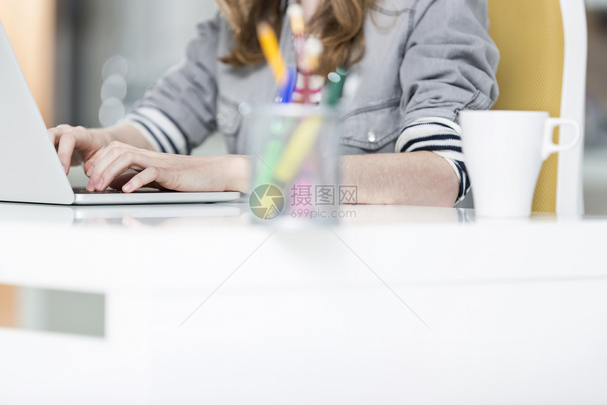 办公室里用笔记本电脑的创意女商人的中段图片