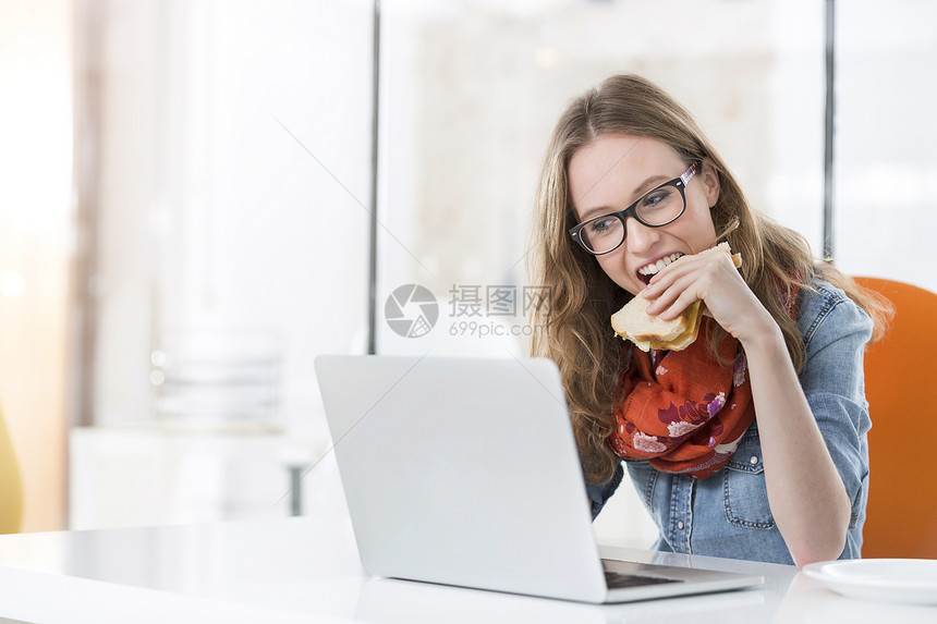 漂亮的女商人办公室用笔记本电脑吃三明治图片