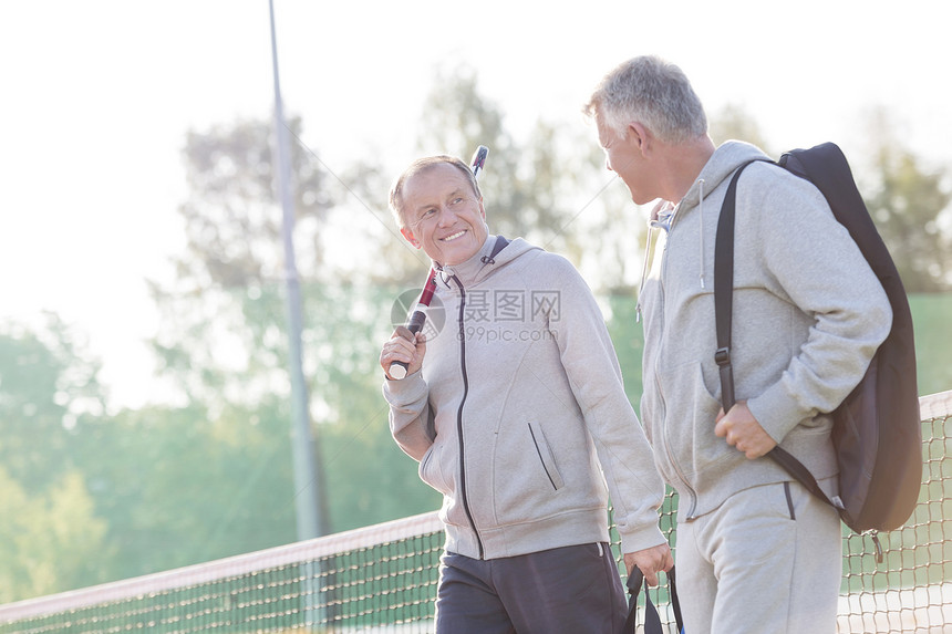 穿着运动服的微笑的男人网球场上散步时说话图片