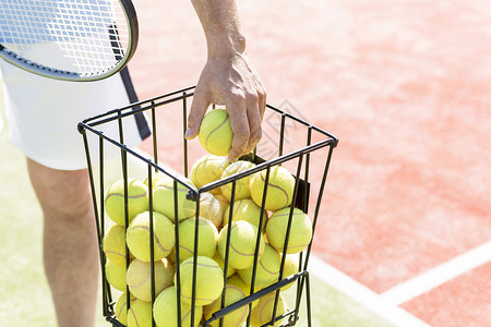 阳光明媚的日子里,男人金属篮子里捡网球的中段高清图片