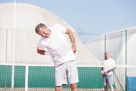 阳光明媚的天,网球比赛中,位腰酸背痛的老人站朋友面前图片
