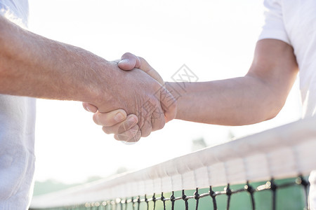 当站网球场面晴朗的天空时,中间的男人握手高清图片
