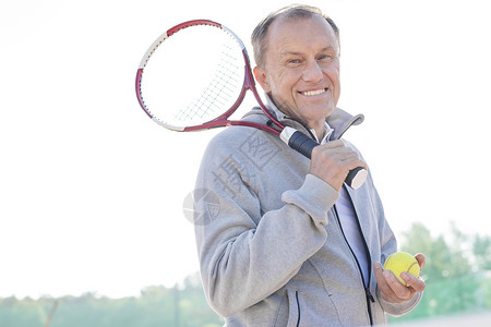 微笑的退休老人的肖像,站网球拍球着晴朗的天空阳光明媚的日子背景图片
