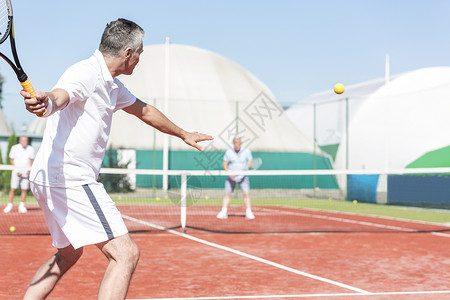 男子夏季周末红场打双打比赛时挥动网球拍背景图片