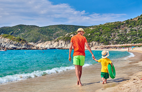 两岁的蹒跚学步的男孩父亲海滩上散步,着充气戒指暑假家庭假期希腊西索尼亚背景图片