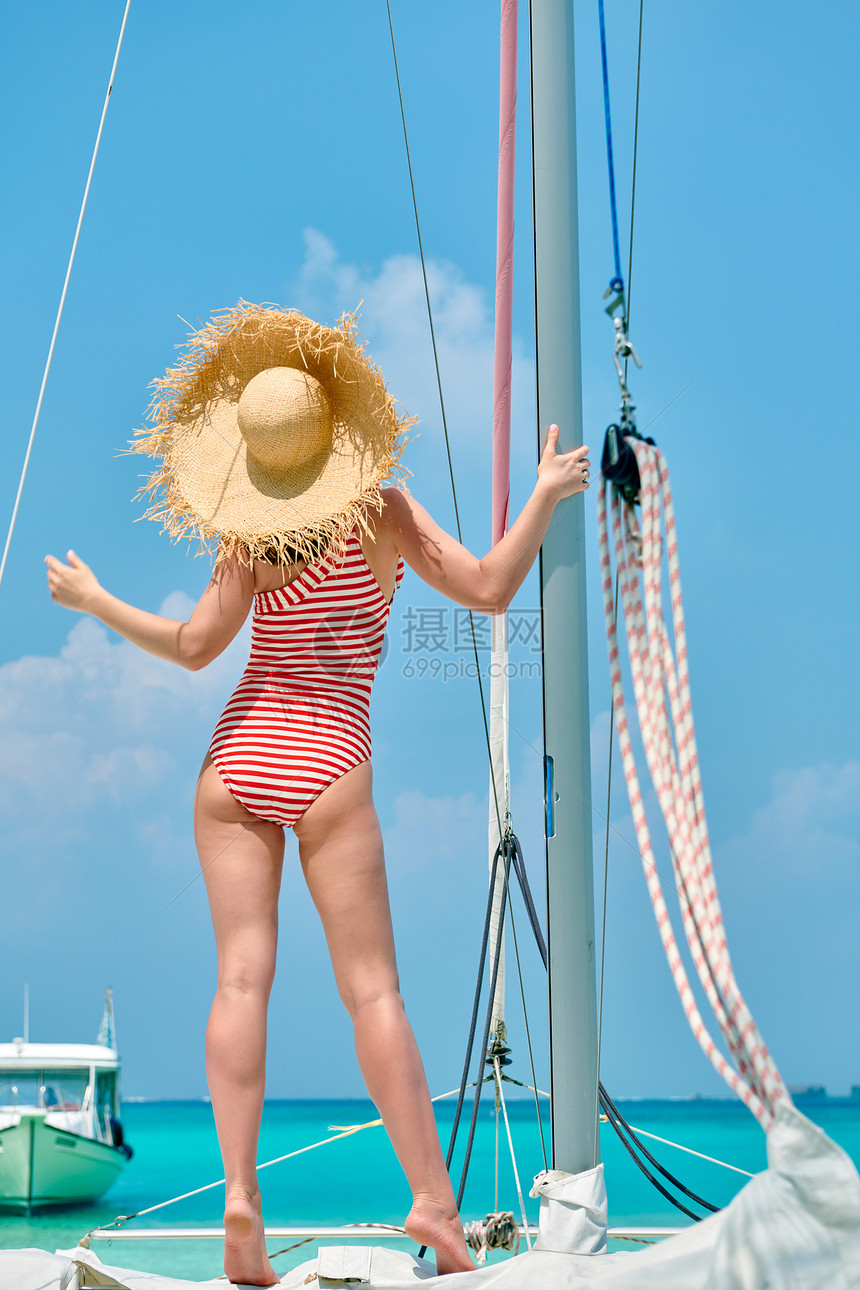 穿着红色条纹单件泳衣的女人站船头马尔代夫的暑假图片