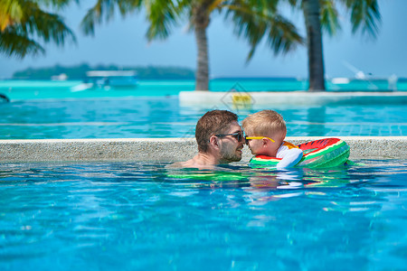 三岁的蹒跚学步的男孩度假游泳池爱斯基摩吻他的父亲马尔代夫的暑假家庭假期背景图片