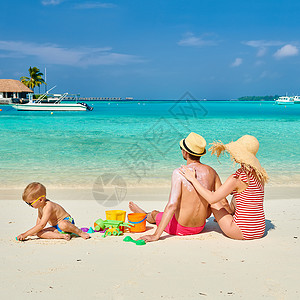 保护海洋孩子海滩上的家人,三岁男孩的轻夫妇女男背部涂防晒霜马尔代夫的暑假背景