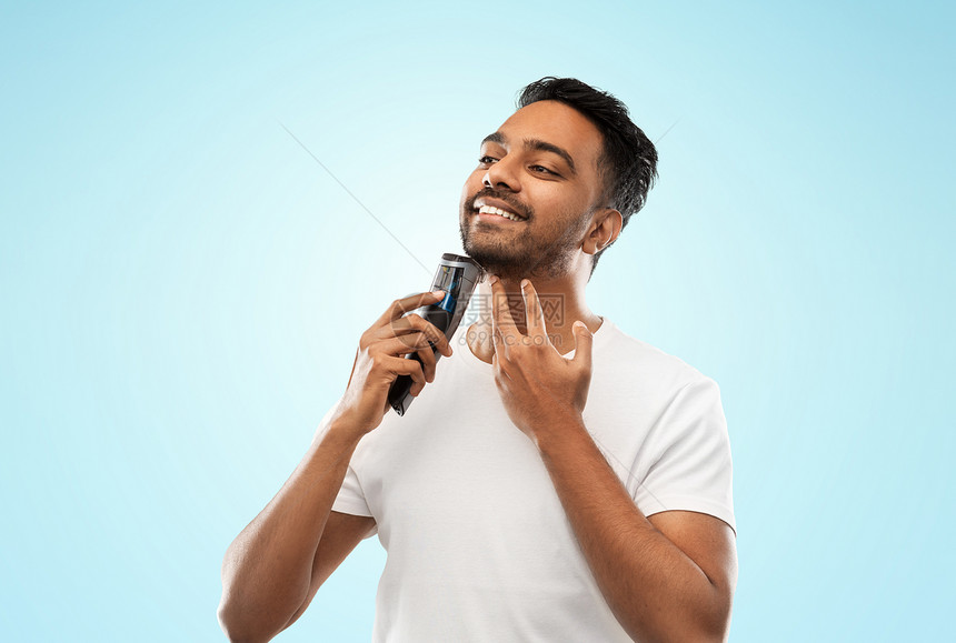 美容,技术人的微笑的印度男子剃须胡须与修剪蓝色背景微笑的印度男人用修剪器刮胡子图片
